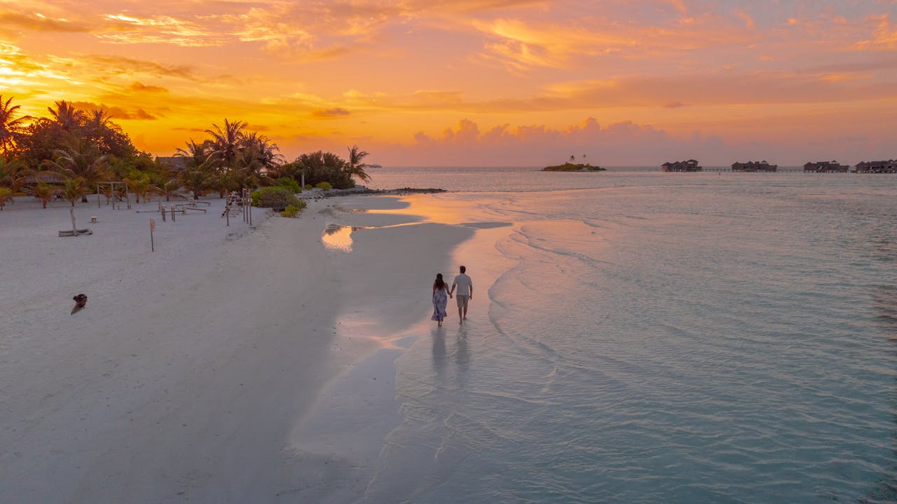A couple walks on a serene Maldivian beach at sunset, capturing romance and tranquility.